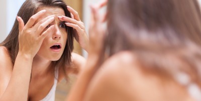 Una joven se toca el acné de la cara mientras se mira en el espejo