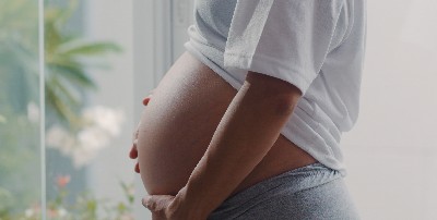Mujer embarazada se toca el vientre frente a una cristalera